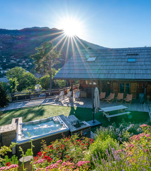 Un chalet de montagne avec sa terrasse en bois et sur la belle pelouse verte un jacuzzi