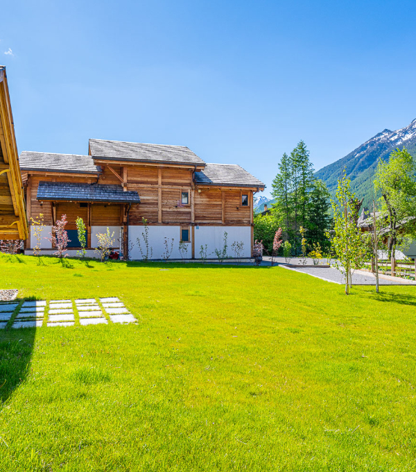 Une magnifique pelouse verte avec au fond un chalet de montagne en bois et un terrain de pétanque à Serre-Chevalier