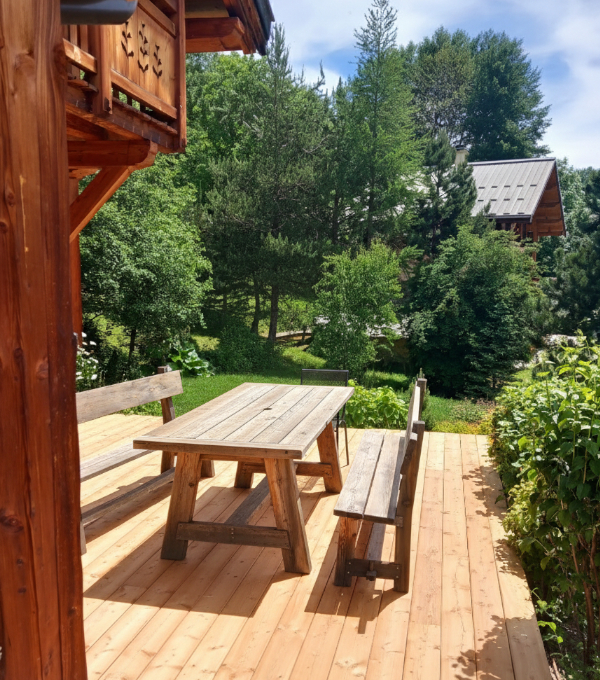 Sur une belle terrasse en bois, une table et des chaises en bois également devant un magnifique chalet de montagne